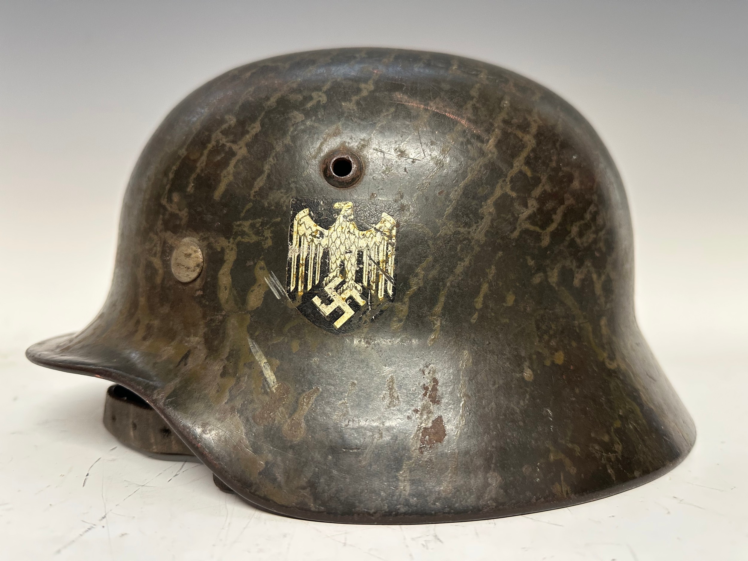 WW2 Third Reich M35 Heer Single Decal Steel Helmet. Former double decal example with the National Colours decal carefully removed as per 1940 regulations. Formally fitted with a camo net. Shell is maker and size marked "EF66". Lot number 4655. Early style alloy liner band with square bales, leather liner and complete with original chinstrap which is maker marked "R. Ehrhardt, Poessneck 1941" with grey painted steel buckle. New to the market.