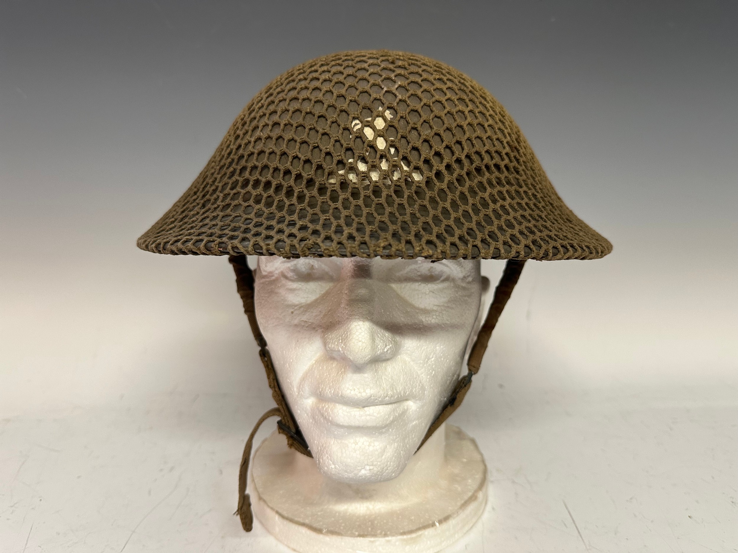 WW2 British Steel Helmet with insignia of the Royal West Kents painted to the front. Complete with size 7 1/4 liner maker marked "BMB" and dated 1 40 and complete with webbing chinstrap. Fitted with a camo net.