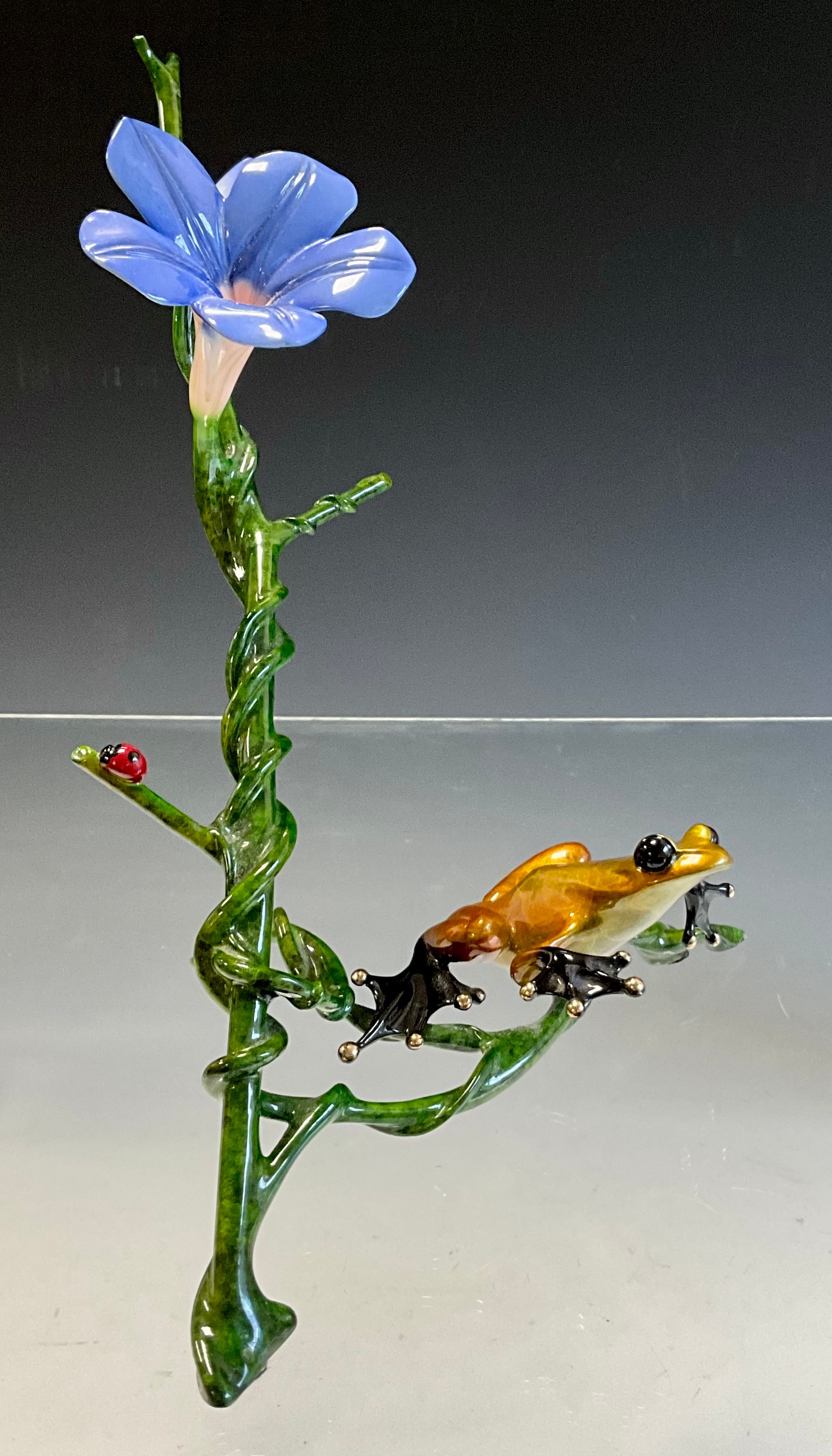 Tim 'Frogman' Cotterill; a limited edition lost wax cast bronze model 'Morning Glory', of a frog with a golden hue patina, resting on the stem of a periwinkle blue flower, 323/2000, signed, numbered and impressed on the underside, approx 25cm x 20cm, with certificate Mulberry Hall, 22/08/11